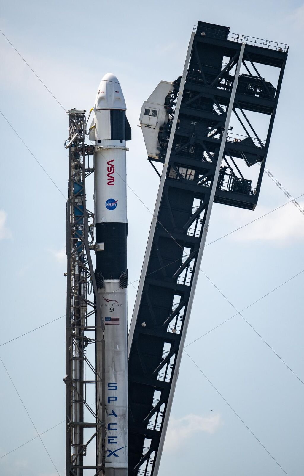 Foguete Falcon 9 com a cápsula Dragon ao lado da torre de lançamento