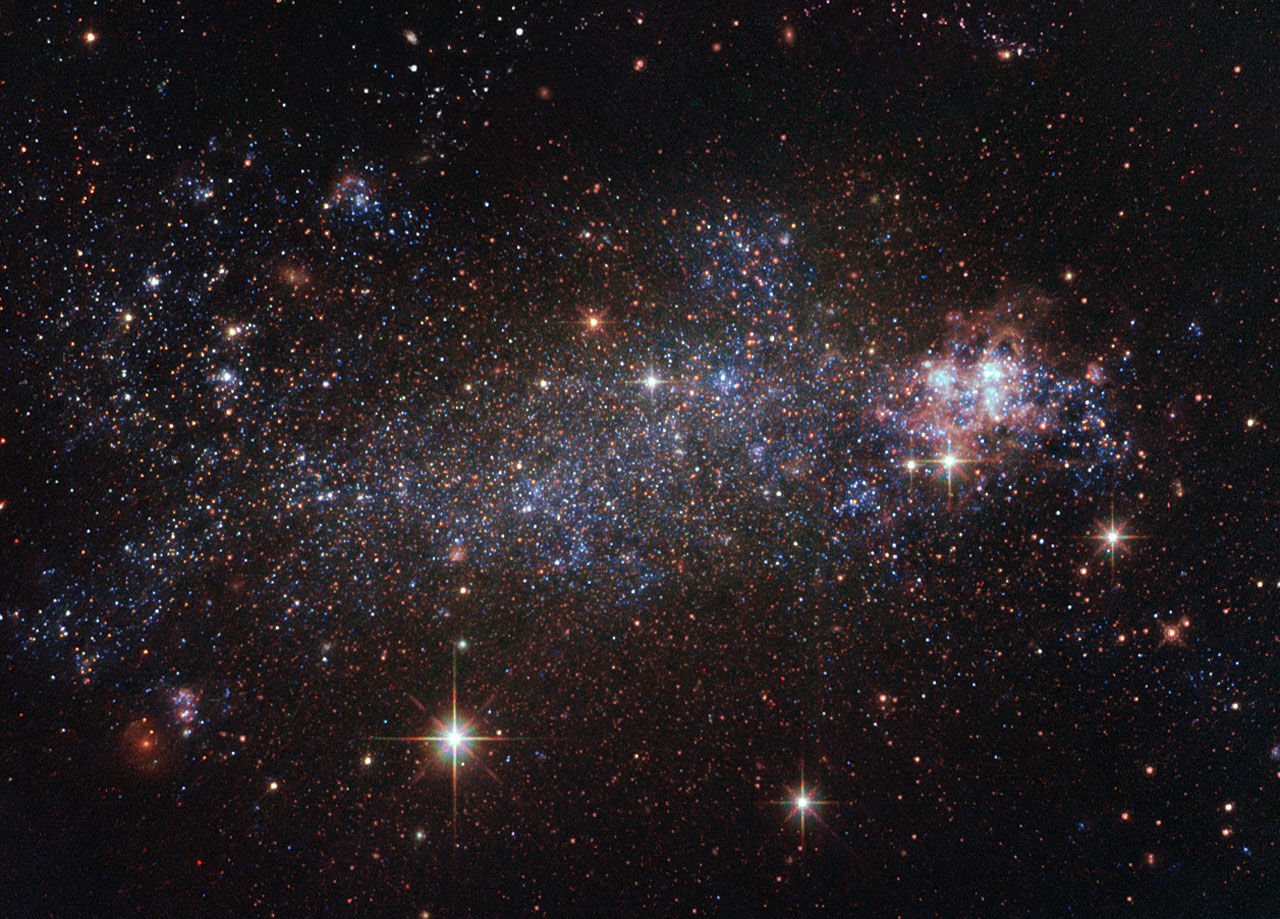 Galáxia anã irregular com muitas estrelas azuis e avermelhadas espalhadas
